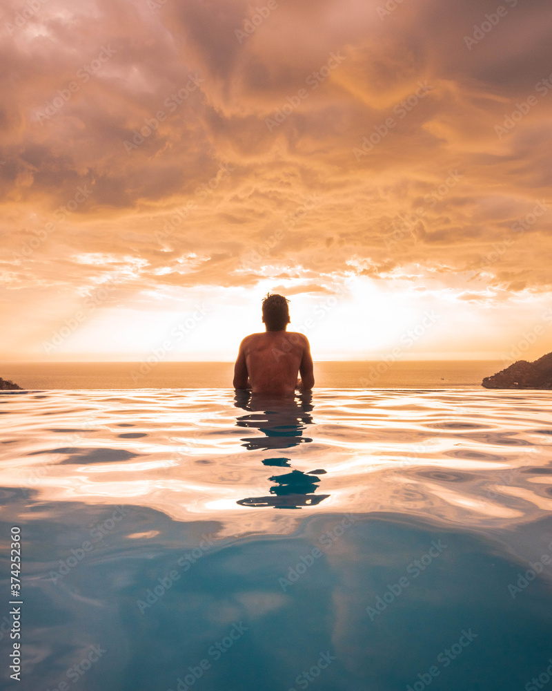 silhouette of a person on the beach watching the sunset on a infinite pool