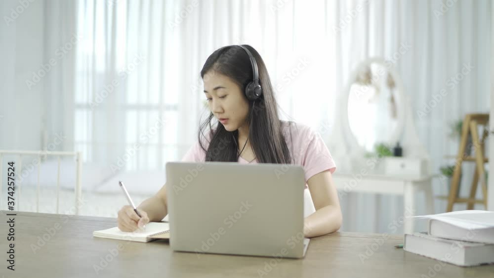 Young Asian woman wears headset conference calling on laptop talks with online teacher studying, working from home. Lady student e learning using computer webcam