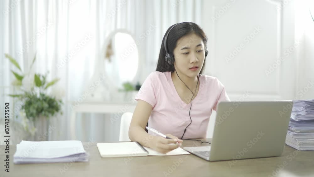 Young Asian woman wears headset conference calling on laptop talks with online teacher studying, working from home. Lady student e learning using computer webcam Young Asian woman wears headset conference calling on laptop talks with online teacher studying, working from home. Lady student e learning using computer webcam