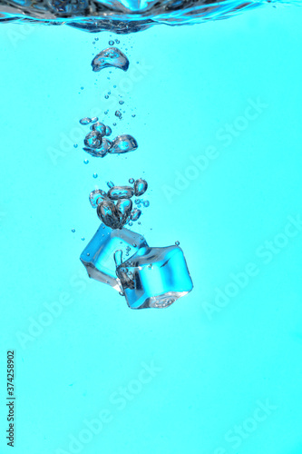 Falling of ice cubes into water on color background