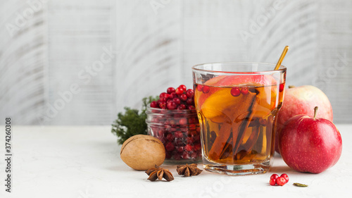 Banner autumn food photo with hot tea with cinnamon, lemon, Apple, berries and spices in a transparent Cup. Copy space.