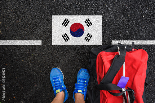 a man with a shoes and travel bag is standing on asphalt next to flag of South Korea and border