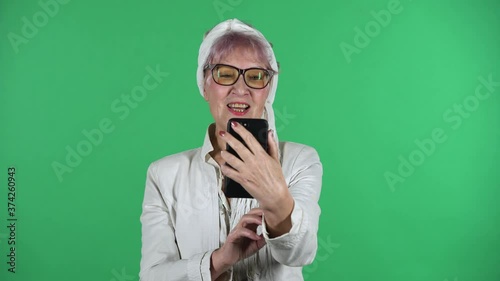 Portrait of old stylish woman is talking for video chat using mobile phoneisolated over green background. photo