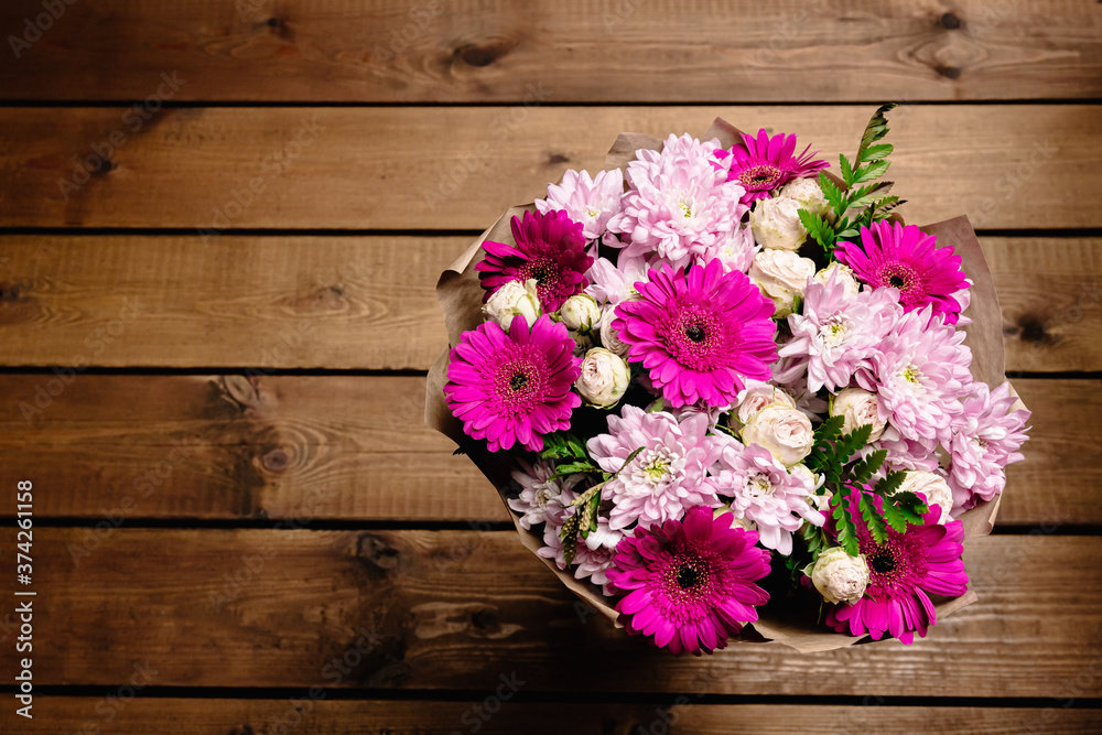 A large beautiful bouquet of chrysanthemums, gerberas, roses and ferns in pink and purple colors wrapped in brown craft paper on a wooden background. Postcard for the holiday. Close-up A large beautiful bouquet of chrysanthemums, gerberas, roses and ferns in pink and purple colors wrapped in brown craft paper on a wooden background. Postcard for the holiday. Close-up