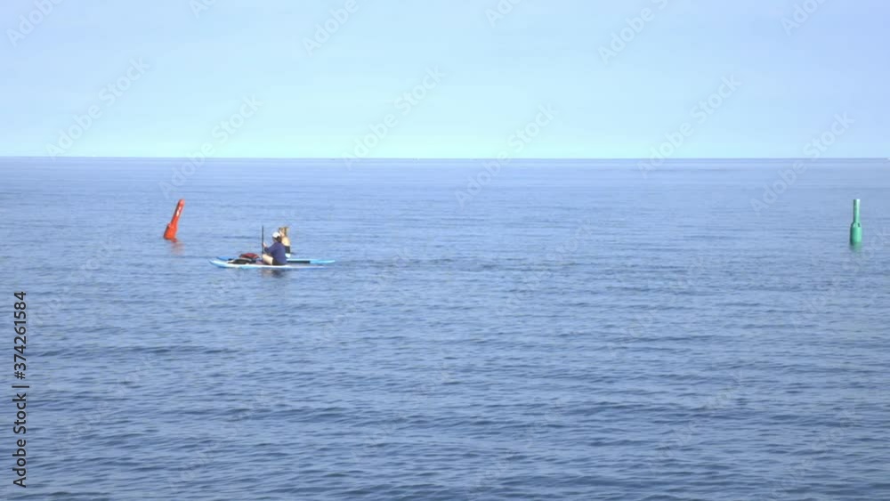 Two Women Sitting On Surf Boards Paddling By Calm Blue Sea On A Sunny Day - Wide Shot (Slow Motion) Two Women Sitting On Surf Boards Paddling By Calm Blue Sea On A Sunny Day - Wide Shot (Slow Motion)