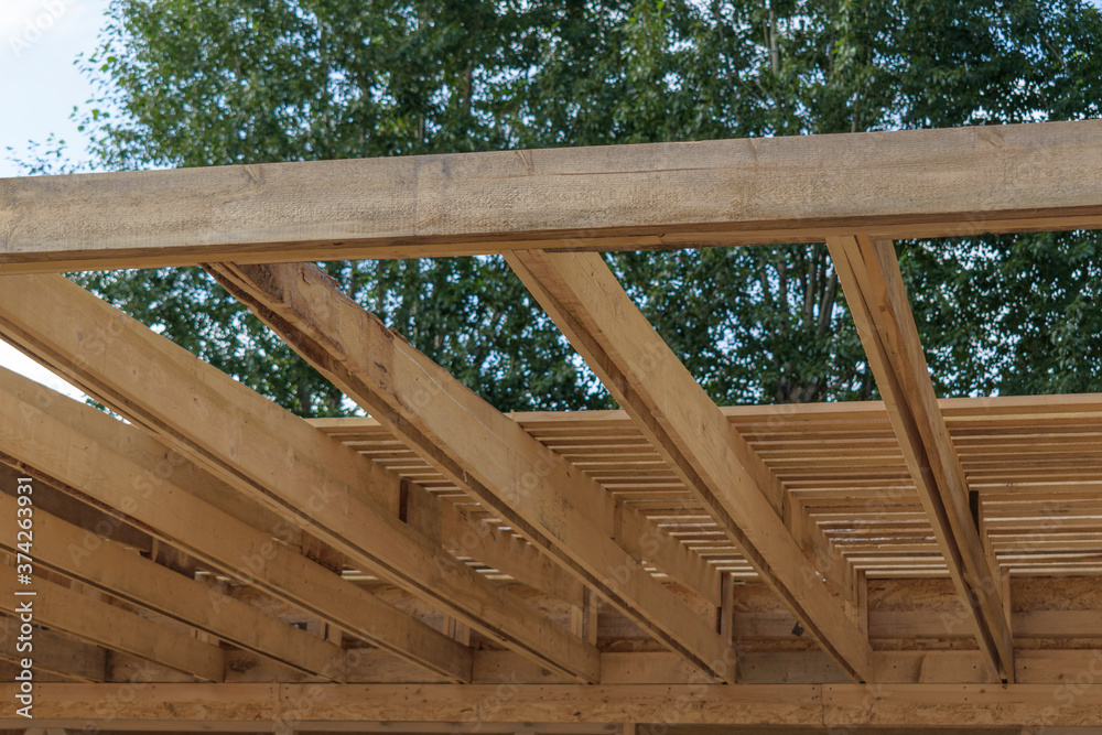 Construction of a lightweight roof from boards. Close-up. Small slope of the rafters. Background - green tree, sky. The concept of building a canopy, barn.