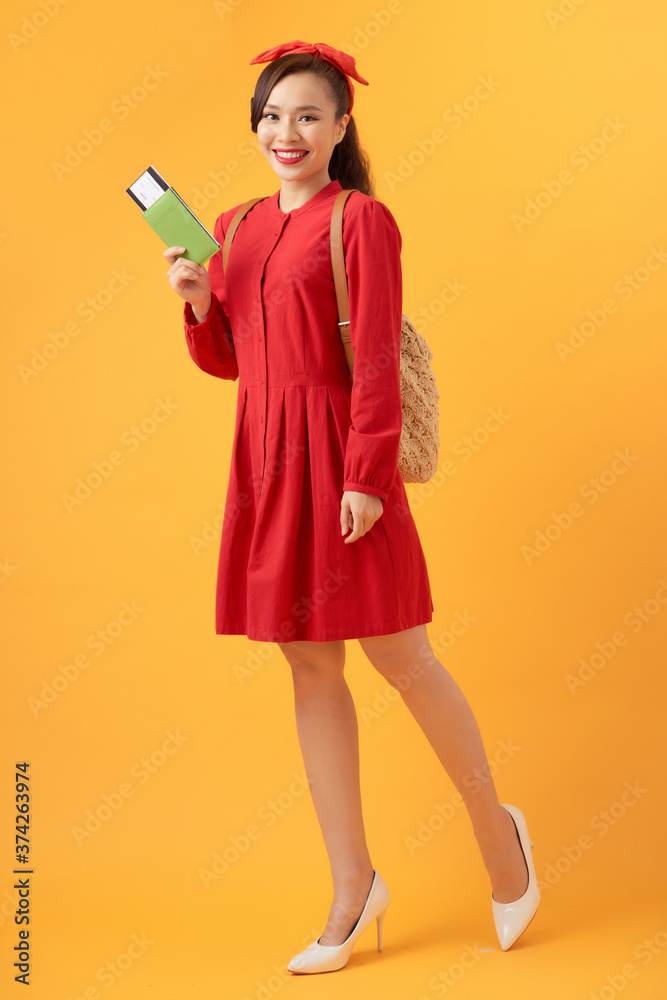 Young Asian woman wearing backpack and holding flight ticket over orange background Young Asian woman wearing backpack and holding flight ticket over orange background