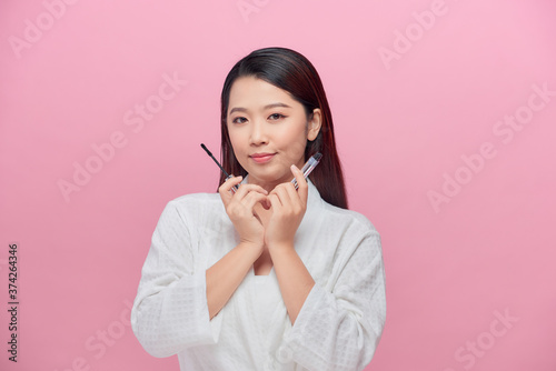 Pretty lady smiling isolated on pink background hold mascara in hands