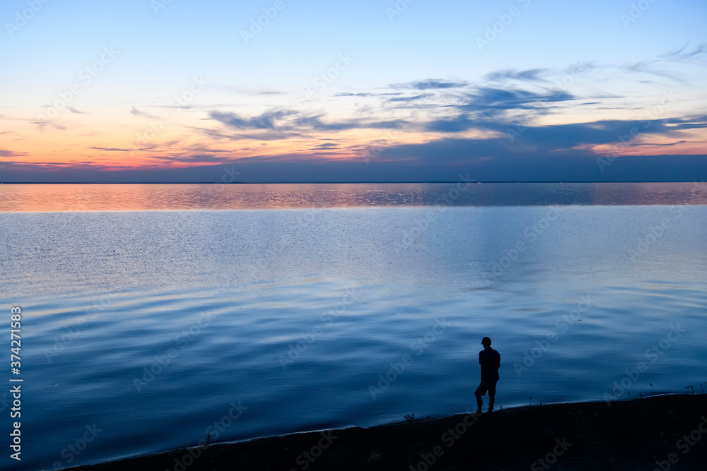 Lonely silhouette of a man standing by the sea at sunset Lonely silhouette of a man standing by the sea at sunset