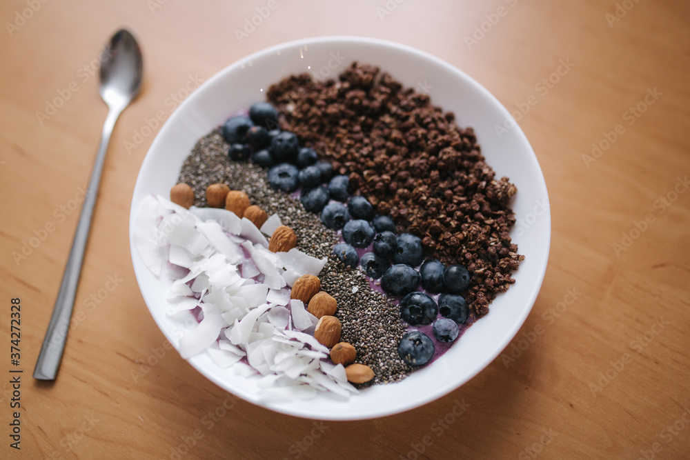 Fresh smoothie bowl with blueberry, chia seeds, almonds, coconut flakes and chocolate flakes. Morning breakfast on wooden table. Lactose free yogurt Fresh smoothie bowl with blueberry, chia seeds, almonds, coconut flakes and chocolate flakes. Morning breakfast on wooden table. Lactose free yogurt