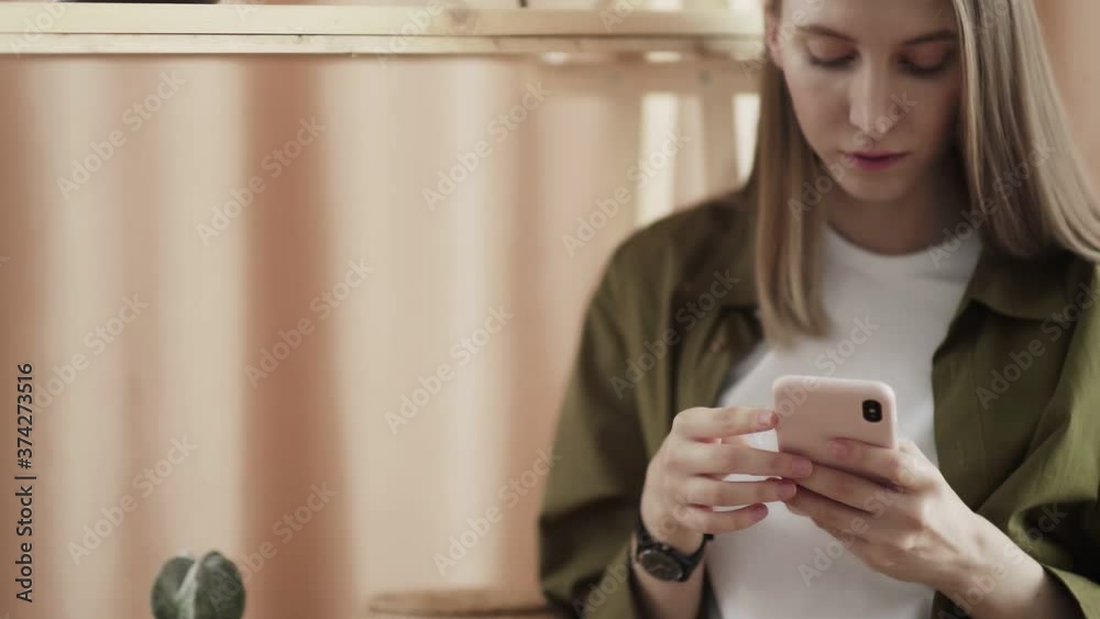 Young woman uses phone near the shelf with flowers Young woman uses phone near the shelf with flowers