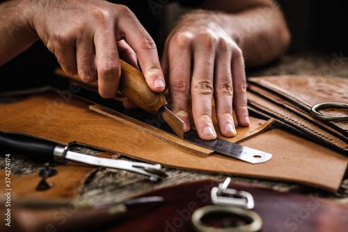 Close up of a shoemaker or artisan worker hands. Leather craft tools on old wood table. Leather craft workshop. photo