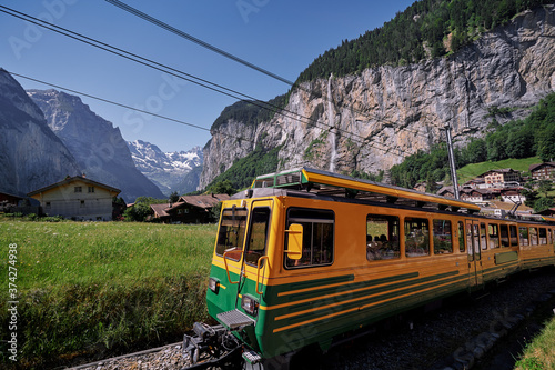 Beautiful mountains landscape. Yellow-green train running through the Swiss Grindelwald Village, Switzerland.