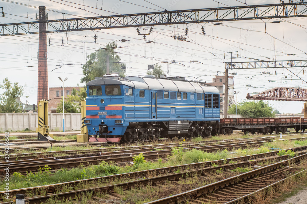 Blue shunting locomotive rides through industrial area.