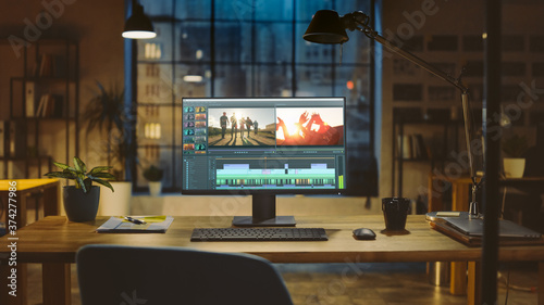 Shot of a Desktop Computer Standing on a Desk with Professional Video Montage Editing Software. In the Background Warm Evening Lighting and Open Space Studio with City Window View. photo