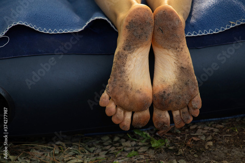 dirty cracked feet of a girl who lies on a mattress in the forest