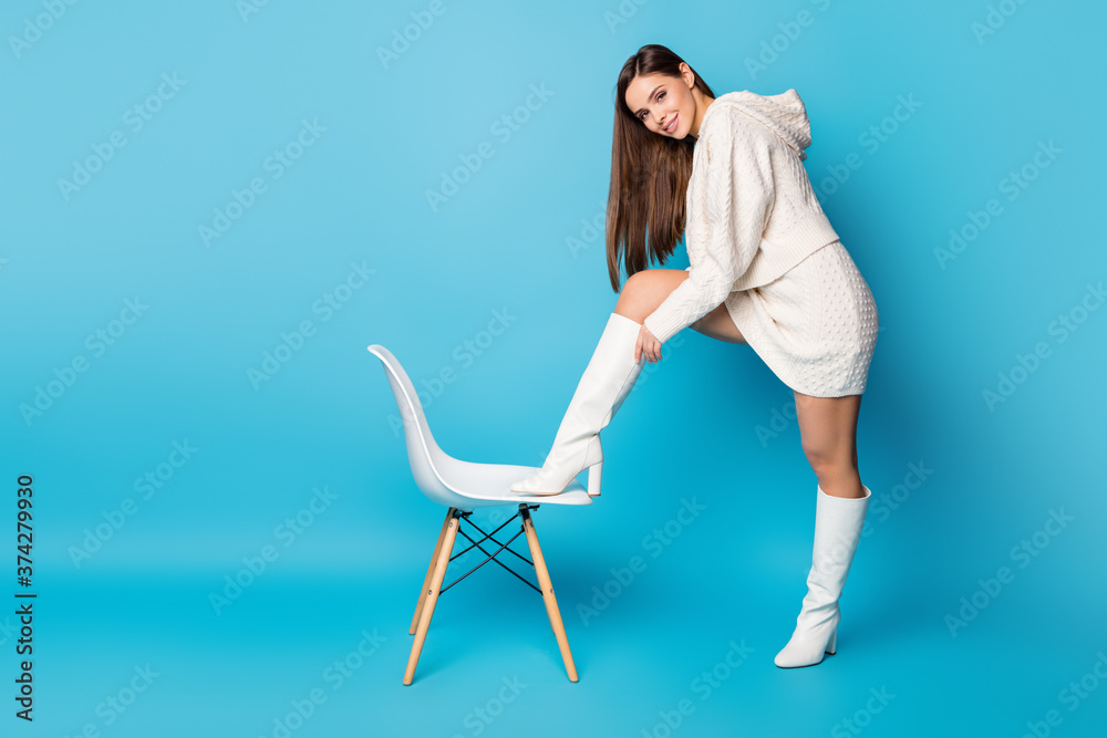 Full boy photo of charming sweel pretty nice girl put her foot on chair try new boot she buy in shopping store mall wear trend clothes isolated over blue color background Full boy photo of charming sweel pretty nice girl put her foot on chair try new boot she buy in shopping store mall wear trend clothes isolated over blue color background
