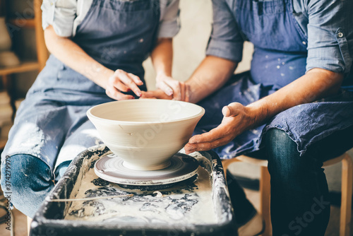 Couple in love working together on potter wheel in craft studio workshop.