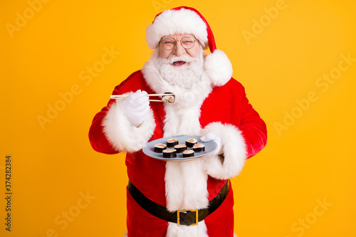 Portrait of his he nice cheerful white-haired Santa enjoying eating domestic gourmet sushi roll maki lunch oriental cuisine isolated bright vivid shine vibrant yellow color background