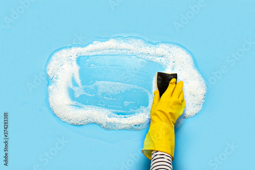 Hand in a yellow rubber glove holds a cleaning sponge and wipes a soapy foam on a blue background. Cleaning concept, cleaning service. Banner. Flat lay, top view photo
