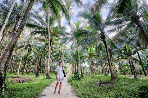 Tropical vacation. Young woman in hat enjoying the view of beautiful coconut palms plantation. photo