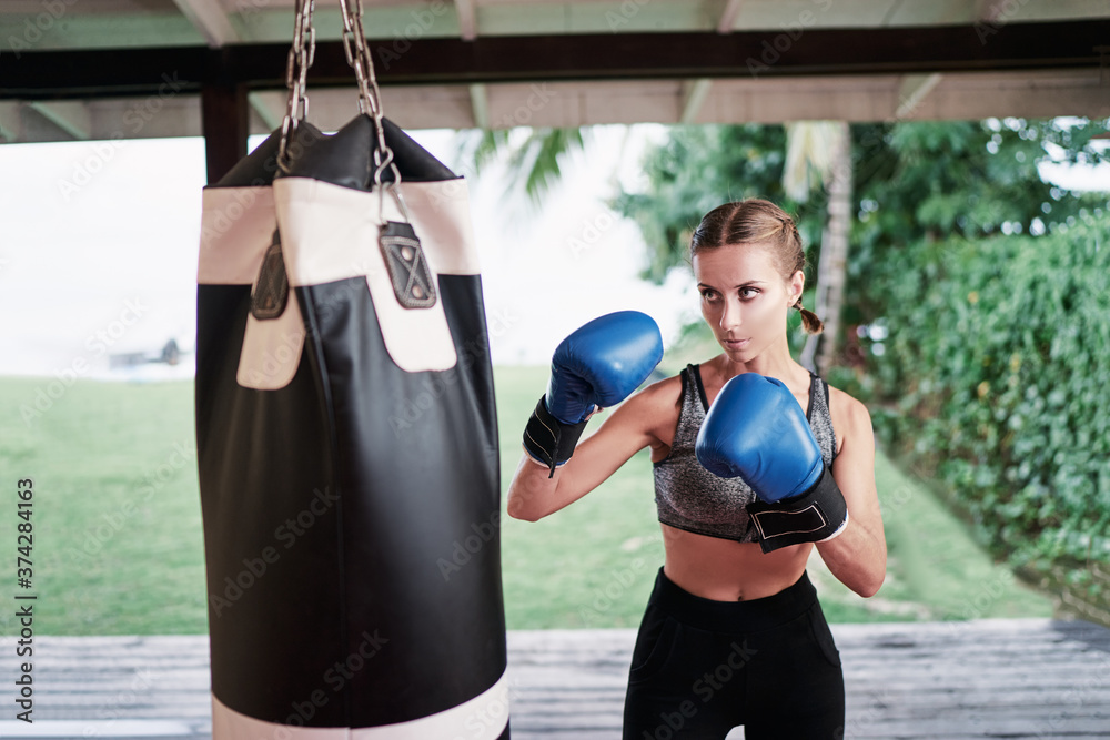 Female boxer hitting a huge punching bag at a gym. Woman boxer training hard.