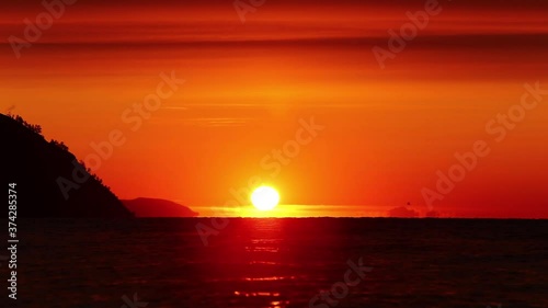 Disk of the sun rising up behind the horizon of Baikal lake with horizon and shore line