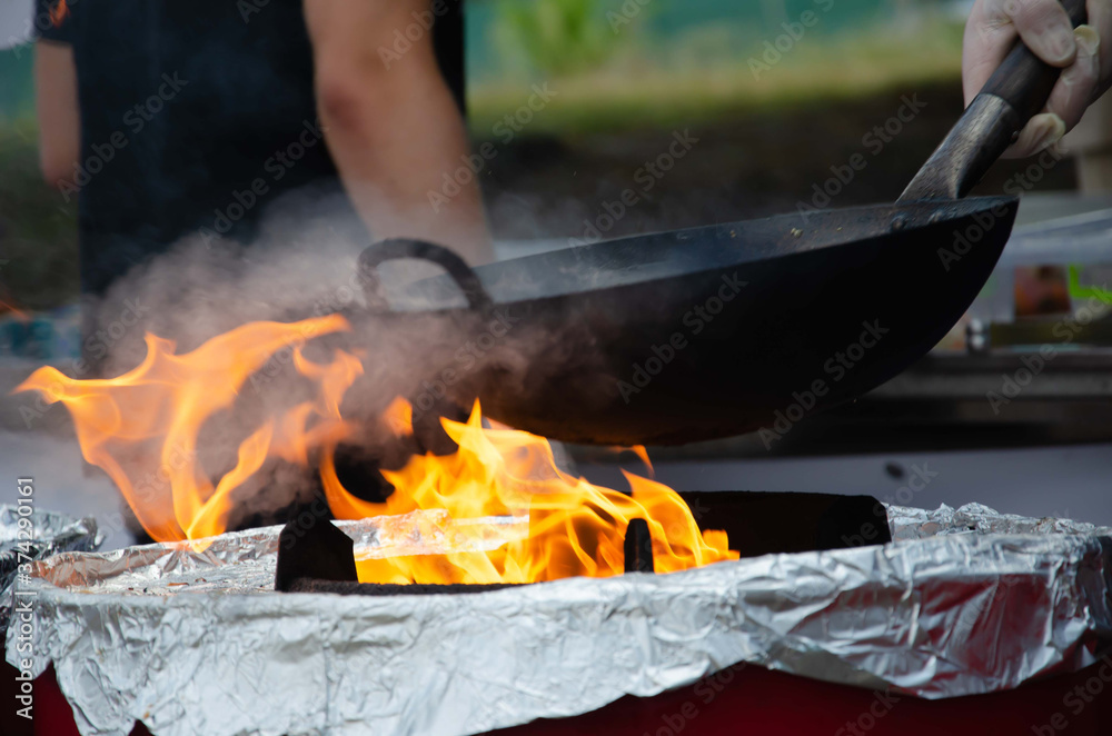 Fire frying pan street food. Chef fire cooking nature.