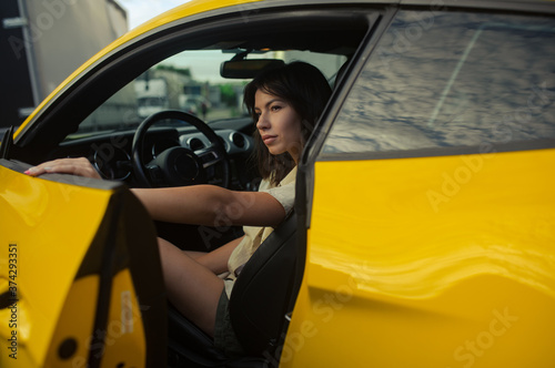 Young woman sits behind the wheel of yellow sport car.
