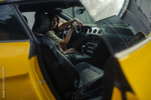 Young woman sits behind the wheel of yellow car.