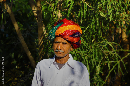 According to Rajasthani culture, an Indian farmer wearing a colorful turban posing in a green garden photo