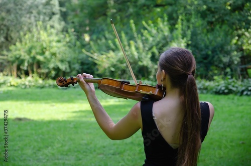 The girl plays the violin rear view. Violinist in a black dress in nature.

