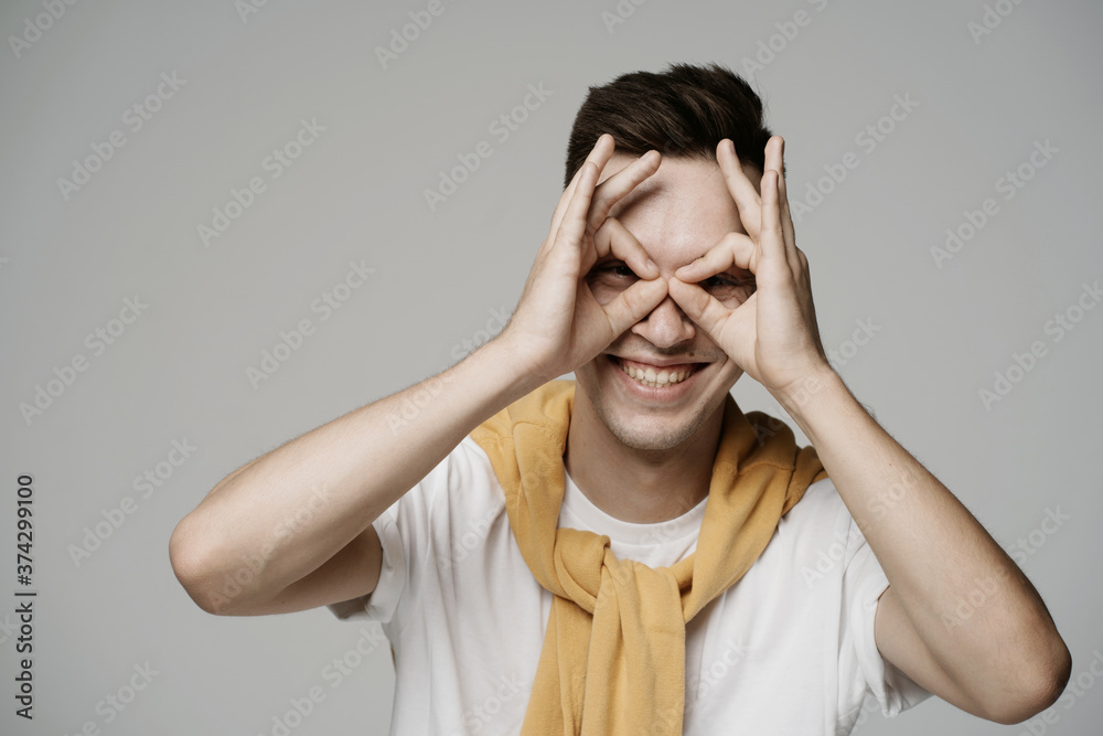 Close-up portrait of a beautiful young guy of Caucasian nationality, smiling, looking at the camera with the fingers of two hands in order of gesture. emotions facial expressions Close-up portrait of a beautiful young guy of Caucasian nationality, smiling, looking at the camera with the fingers of two hands in order of gesture. emotions facial expressions