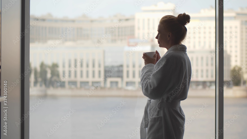 Mature woman in bathrobe holding coffee cup in kitchen at home Mature woman in bathrobe holding coffee cup in kitchen at home