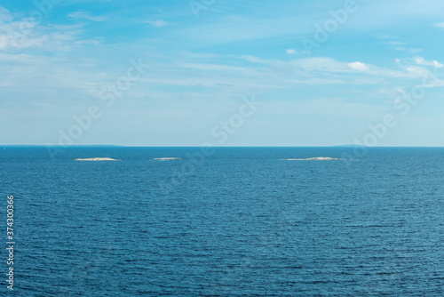 Three little white islands on blue background of water and cloudy sky on Ladoga lake in Karelia