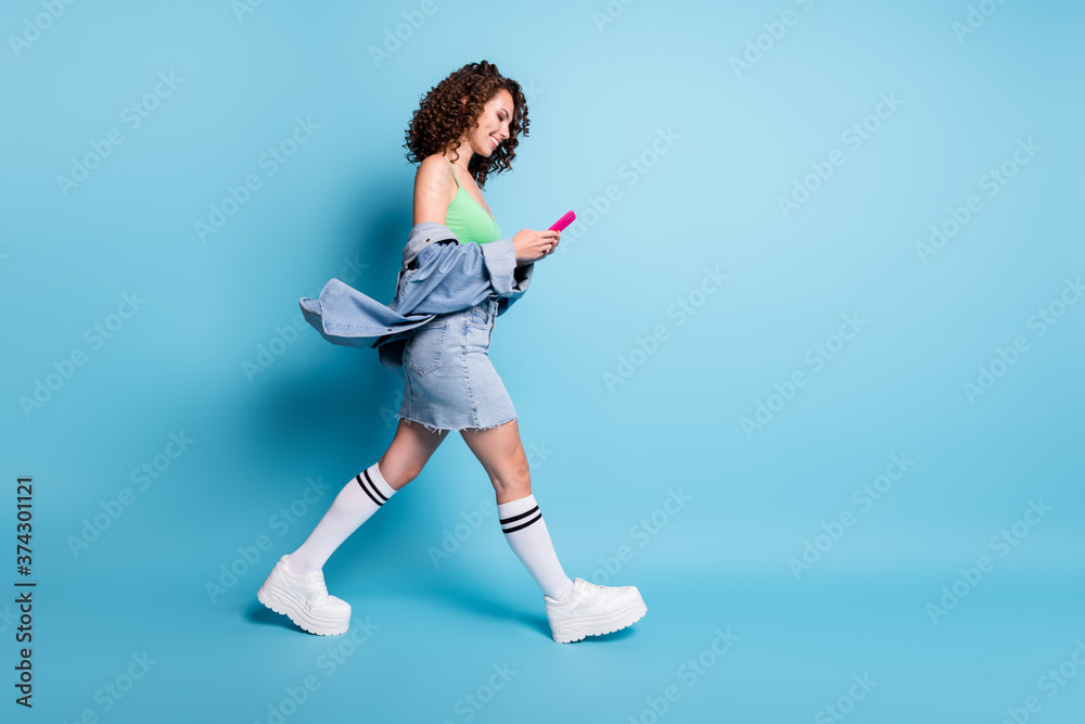 Full length profile side photo of positive girl go walk copyspace use smartphone chatting social media friend travel summer wear green crop top denim isolated blue pastel color background