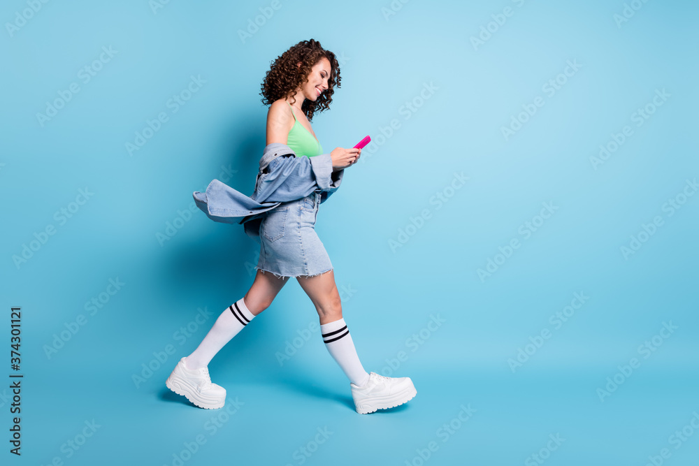 Full length profile side photo of positive girl go walk copyspace use smartphone chatting social media friend travel summer wear green crop top denim isolated blue pastel color background Full length profile side photo of positive girl go walk copyspace use smartphone chatting social media friend travel summer wear green crop top denim isolated blue pastel color background