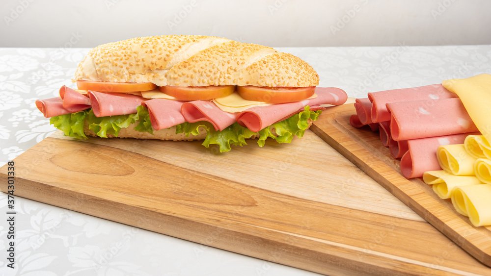 Mortadella sandwich, lettuce, tomato and cheese on a polished board and