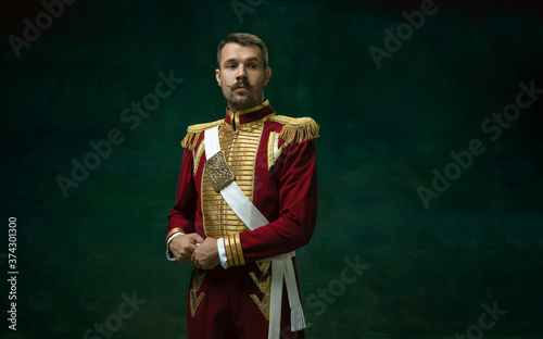 Thoughtful. Young man in suit as Nicholas II isolated on dark green background. Retro style, comparison of eras concept. Beautiful male model like historical character, monarch, old-fashioned.
