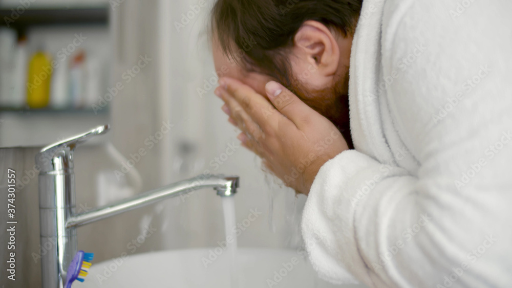 Fototapeta premium Stout man in bathrobe Washing Face in Bathroom at Morning.