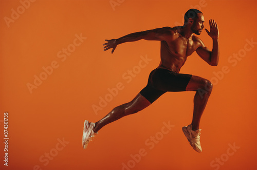 Muscular athlete running on orange background © Jacob Lund