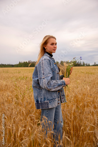 Portrait of a young girl with a bouquet in her hands in a field of rye. © FO_DE