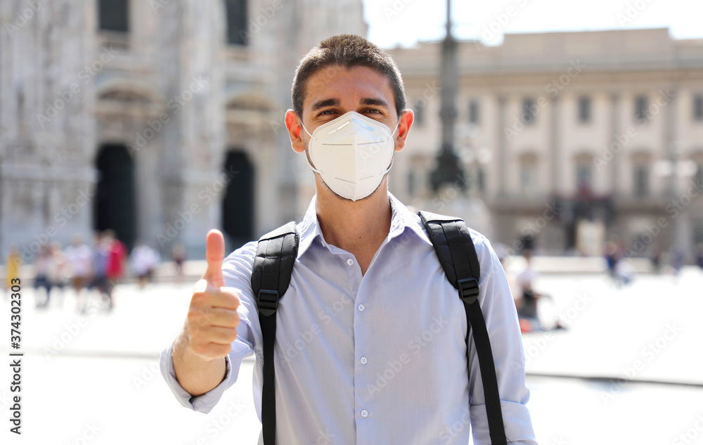 Plakat COVID-19 Optimistic young man wearing protective mask KN95 FFP2 showing thumb up in Milan, Italy