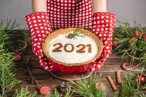 Homemade tart with the number 2021. Wooden table decorated with pine branches and red decor for Christmas and new year