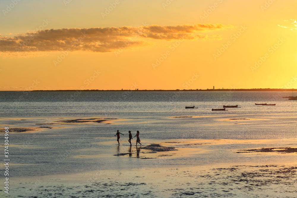 Three childrens are playing in the sea at low tide on a background of amber sunset