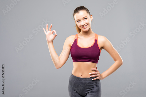 Young happy smiling cheerful woman in sports wear showing OK gesture on gray background © dianagrytsku