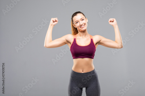 Portrait of fitness woman showing her biceps isolated on a gray background © dianagrytsku