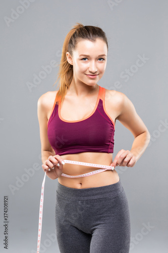 Fitness Woman measuring her body isolated on gray background. Weight loss concepts © dianagrytsku