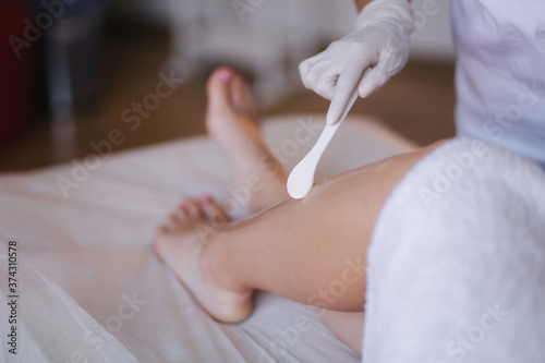 Young woman beautician in mask applies contact gel on the leg of a woman for laser hair removal in medical clinic. Close up