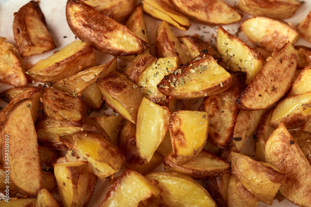Delicious baked potatoes slices with seasoning on white paper close up Delicious baked potatoes slices with seasoning on white paper close up